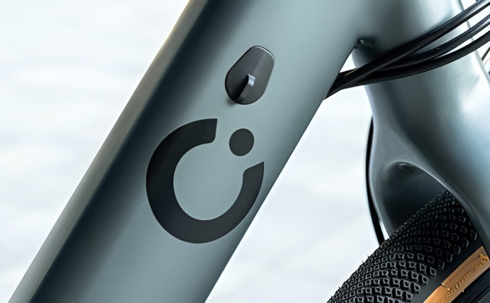 Rower elektryczny CECOTEC Sprint M20 28 cali Szary ściana budynku zbliżenie na baterię w ramie widoczne logo marki zasięg do 70 km bateria litowo-jonowa napięcie 36 V pojemność 10 Ah (360 Wh) czas ładowania około 4-5 godzin żywotność około 1000 ładować umiejscowiona na ramie zintegrowana z konstrukcją roweru