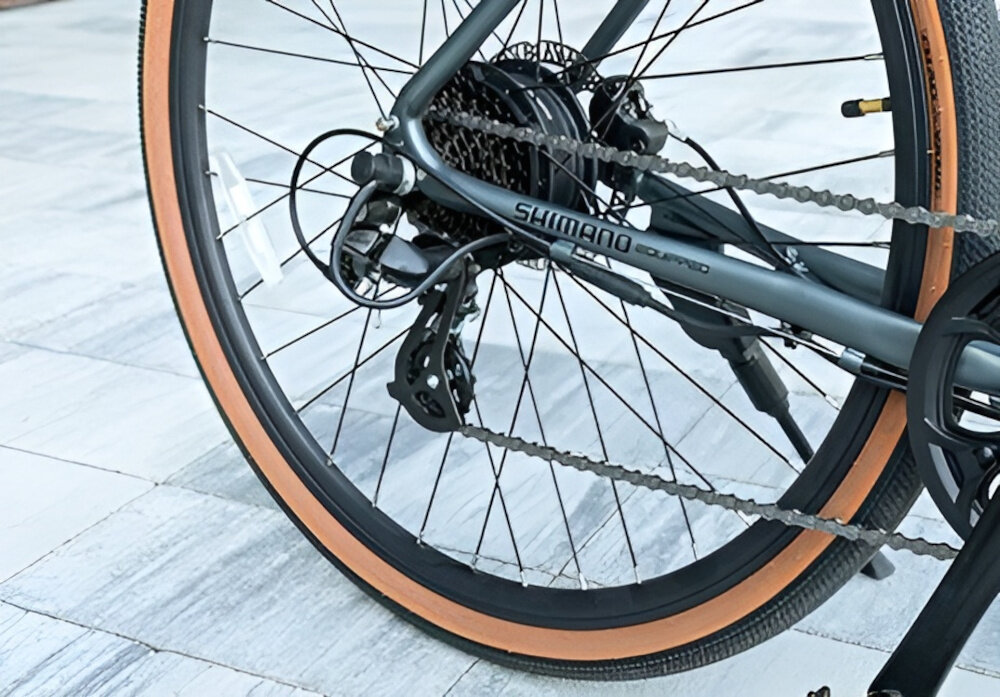 Rower elektryczny CECOTEC Sprint M20 28 cali Szary chodnik ściana budynku zbliżenie na przerzutkę manetki SHIMANO typu SL-M315 8 biegów tylna przerzutka SHIMANO Altus 8S technologię SHADOW przerzutka jest schowana i mniej narażona na uszkodzenia duża wytrzymałość precyzyjne działanie zmiana biegów jest płynna i bezproblemowa