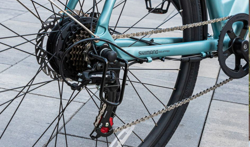 Rower elektryczny CECOTEC Urban Pro M18 28 cali Niebieski chodnik zbliżenie na przerzutkę manetki SHIMANO typu M315 7 biegów tylna przerzutka SHIMANO Tourney duża wytrzymałość precyzyjne działanie zmiana biegów jest płynna i bezproblemowa