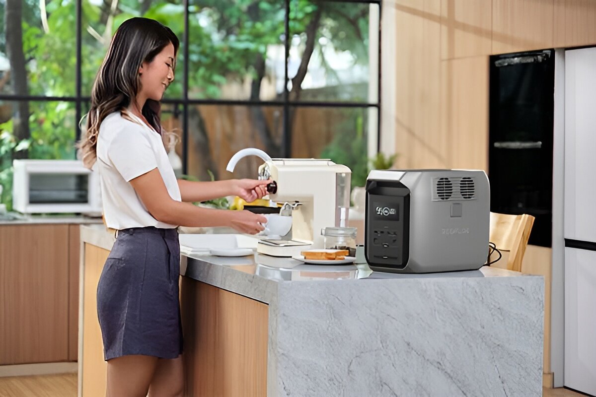 Stacja zasilania ECOFLOW Delta 3 1500 Wh Bank energii, obudowa, odporność, IP54, trwałość,  Kobieta przy kuchennym blacie przygotowuje kawę, obok stacja Delta 3 z widocznym wyświetlaczem.