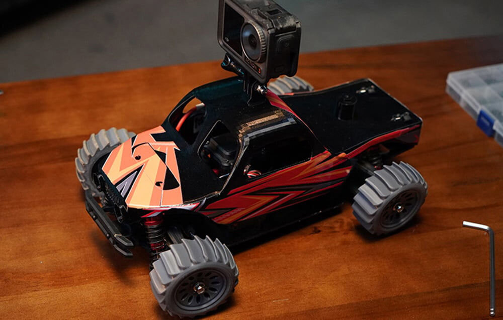 Drukarka 3D ANYCUBIC Kobra S1 Combo prezentacja autka z wydrukowanymi kołami na blacie na samochodziku kamerka sportowa współpraca z filamentami PLA ABS PETG szeroka kompatybilność i możliwości zastosowania