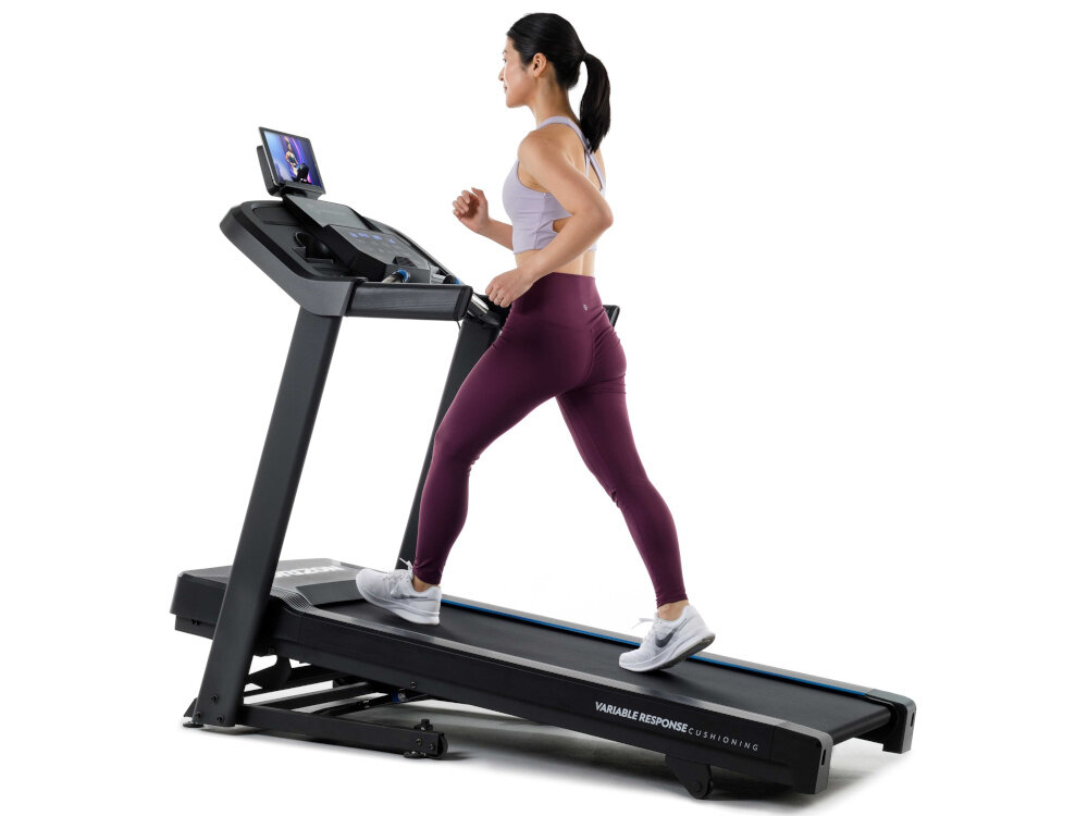 Bieżnia elektryczna HORIZON 5.0AT-21 1864W 16km-h kobieta biegnie na bieżni widok z boku zdjęcie na białym tle elektroniczny kąt nachylenia od 0 do 10% symulacja treningów w warunkach wzniesień zwiększa zaangażowanie mięśni efektywne spalanie kalorii oszczędza czas wygoda