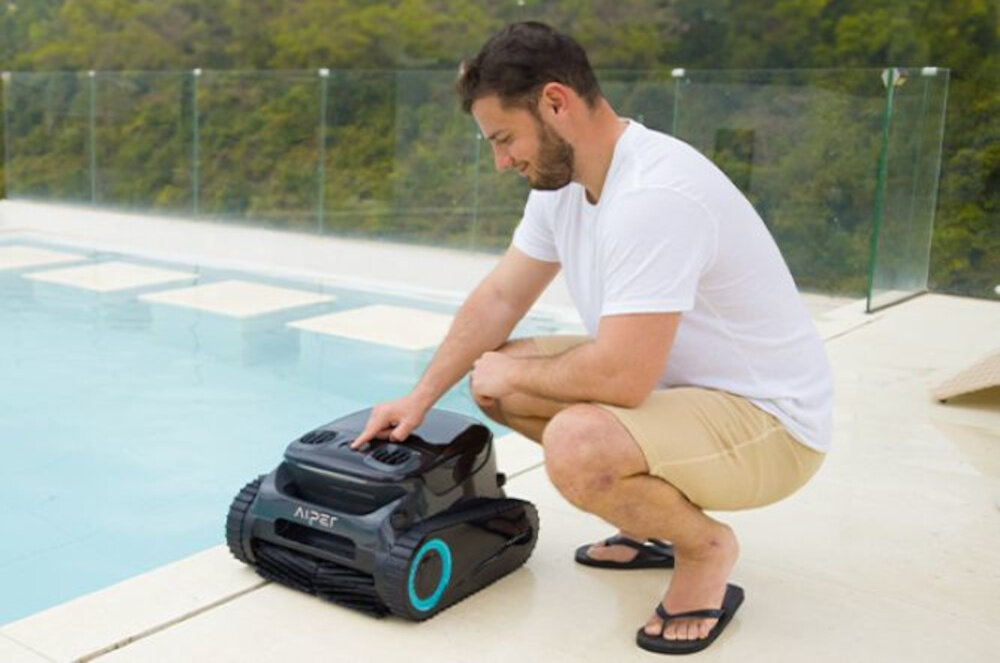 Robot do czyszczenia basenów AIPER Scuba S1 Pro basen osoba kuca obok robota naciska przycisk na korpusie 5 trybów pracy AUTO FLOOR ONLY WALL ONLY ECO WATERLINE przycisk na robocie aplikacja na urządzenia mobilne