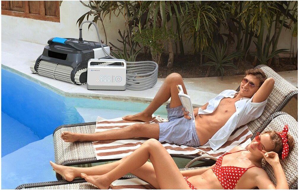 Robot do czyszczenia basenów WYBOT L1, programator, harmonogram, praca, uruchomienie, para leży na leżakach, w tle robot przy krawędzi basenu