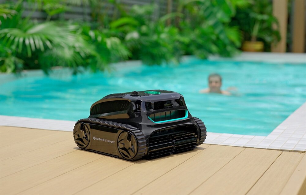 Robot do czyszczenia basenów WYBOT S2, basen, woda, czyszczenie, porządek, osoba pływa w basenie, koło basenu robot frontem lewo skos