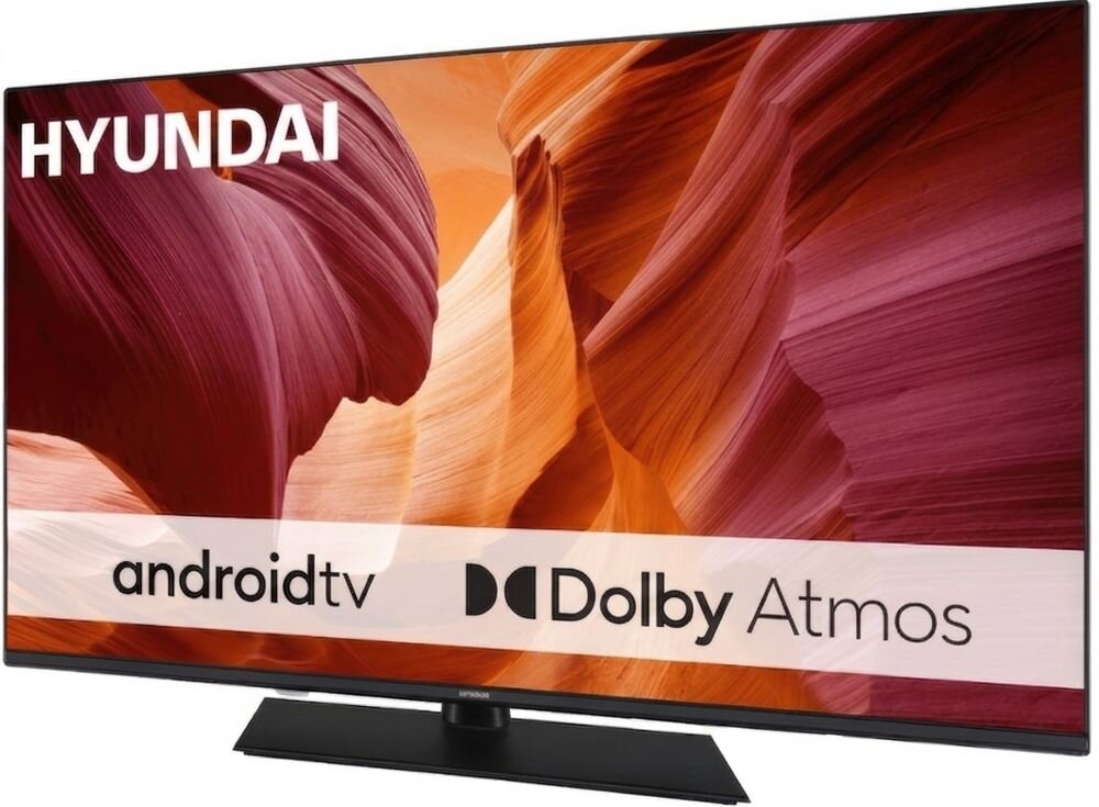 Telewizor z logo HYUNDAI wyświetla obraz przedstawiający kolorowe formacje skalne. Na ekranie widoczne są napisy: \'android tv\' i \'Dolby Atmos\'.