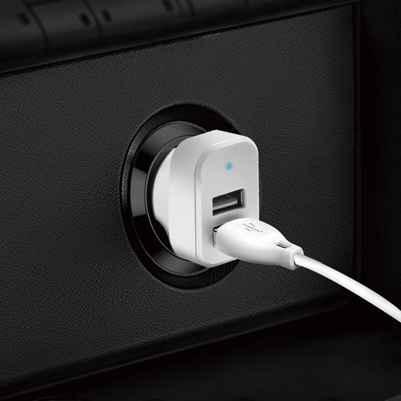 Biała ładowarka samochodowa z dwoma portami USB jest podłączona do gniazda zapalniczki. Do jednego z portów podłączony jest biały kabel USB.