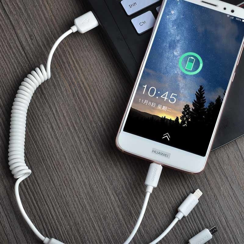 Na drewnianym blacie leży smartfon z widocznym ekranem, na którym jest godzina 10:45 i ikona ładowania baterii. Telefon jest podłączony do białego kabla USB z trzema różnymi końcówkami: Lightning, Typ C i Micro USB.