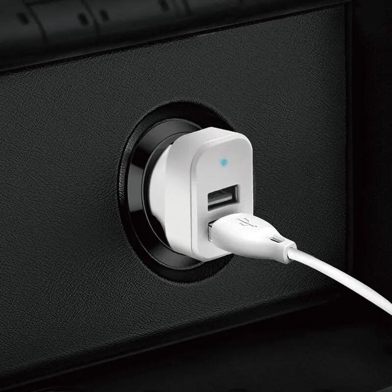 Biała ładowarka samochodowa z dwoma portami USB jest podłączona do gniazda zapalniczki. Do jednego z portów podłączony jest biały kabel USB.