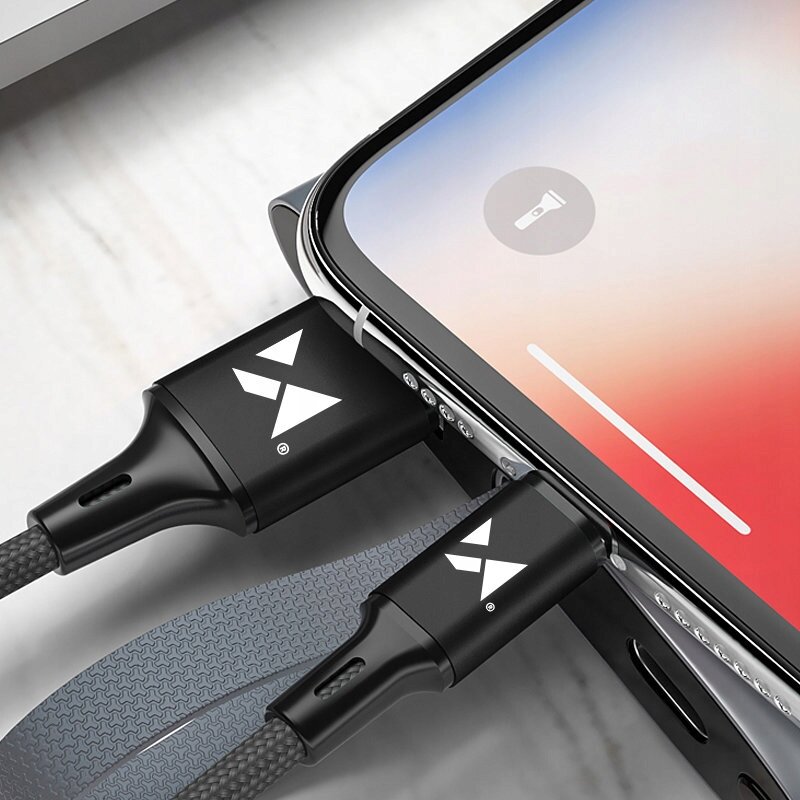 Na obrazie widoczne są dwa czarne kable USB z białym logo w kształcie litery \'X\', podłączone do urządzenia mobilnego. Ekran urządzenia pokazuje ikonę latarki i pasek głośności.
