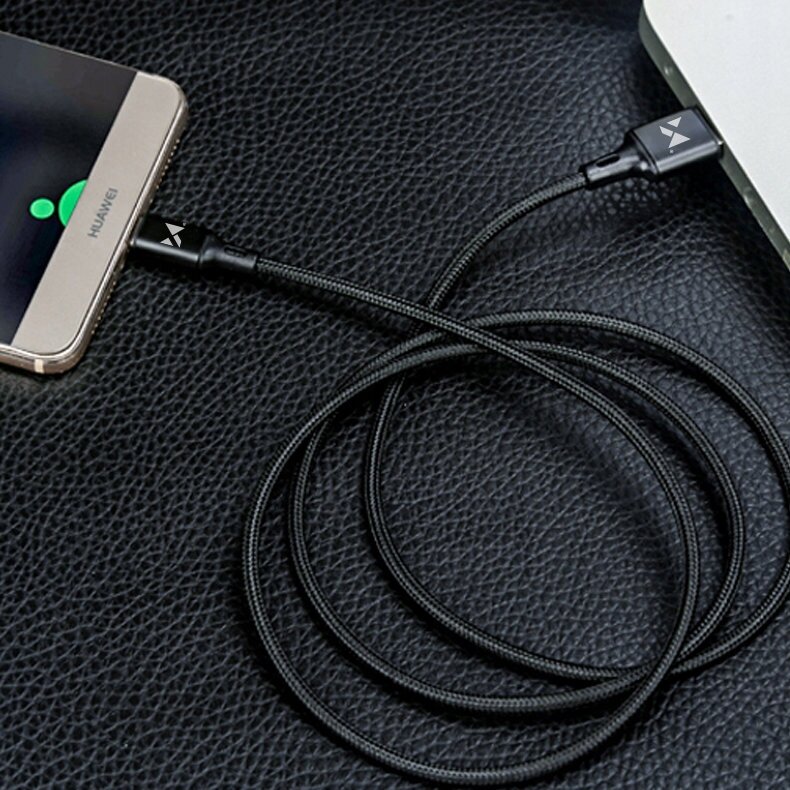 Czarny kabel USB z plecionym oplotem podłączony do smartfona i laptopa, leży na czarnej, teksturowanej powierzchni. Na końcówkach kabla widoczne jest logo w kształcie litery \'V\'.