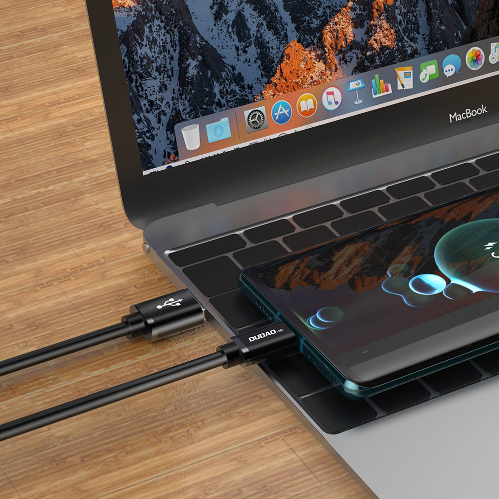 Na obrazie widać laptopa z otwartym ekranem, na którym wyświetlany jest system operacyjny z ikonami aplikacji. Do laptopa podłączony jest czarny kabel USB z napisem \'DUDAO\', który łączy się z urządzeniem mobilnym leżącym na klawiaturze.