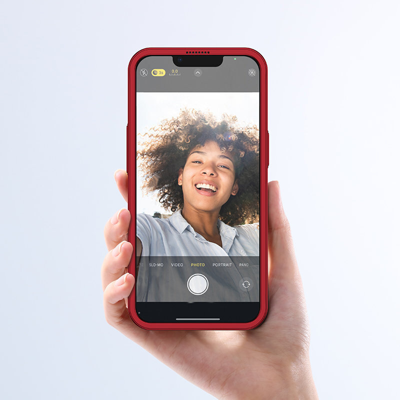 Osoba trzyma smartfon w czerwonym etui, na ekranie widoczna jest aplikacja aparatu z włączonym trybem \'PHOTO\'.