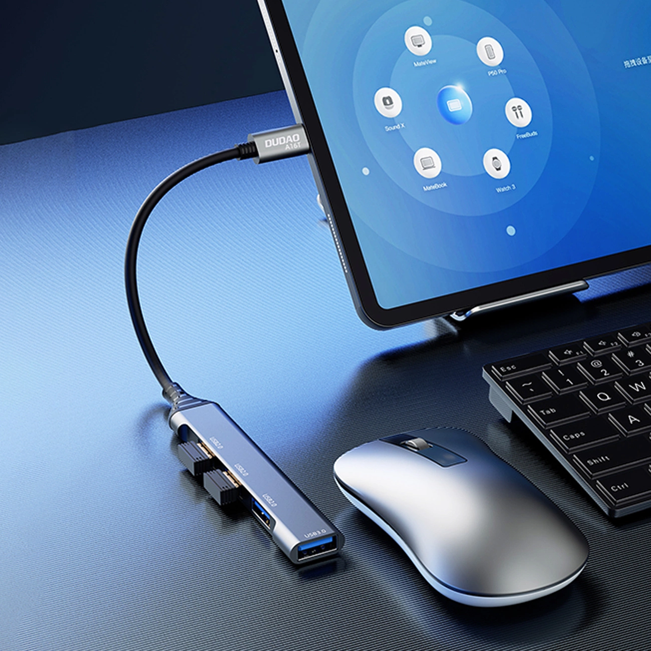 Na obrazie widoczny jest czarny hub USB-C marki Dudao z czterema portami USB-A, podłączony do tabletu. Obok znajdują się myszka i klawiatura na metalicznym tle.