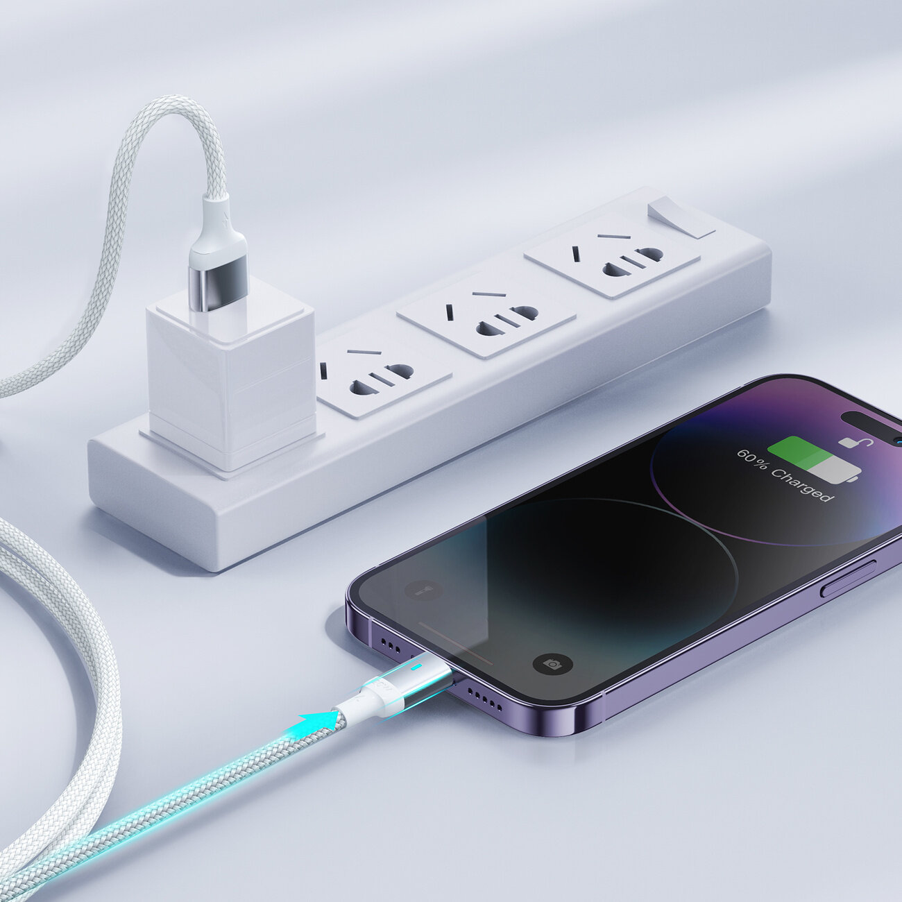 Na obrazie widać telefon podłączony do kabla USB/Lightning, który jest wpięty do listwy zasilającej. Na ekranie telefonu widoczny jest wskaźnik naładowania z napisem \'60% Charged\'.