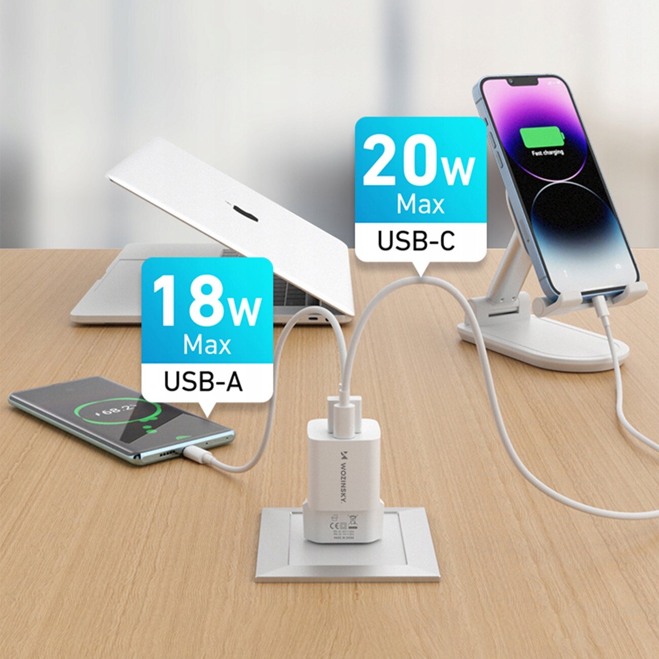 Na drewnianym blacie znajduje się ładowarka sieciowa z dwoma kablami podłączonymi do urządzeń: telefonu i laptopa. Obok ładowarki widoczne są oznaczenia \'18W Max USB-A\' i \'20W Max USB-C\'.