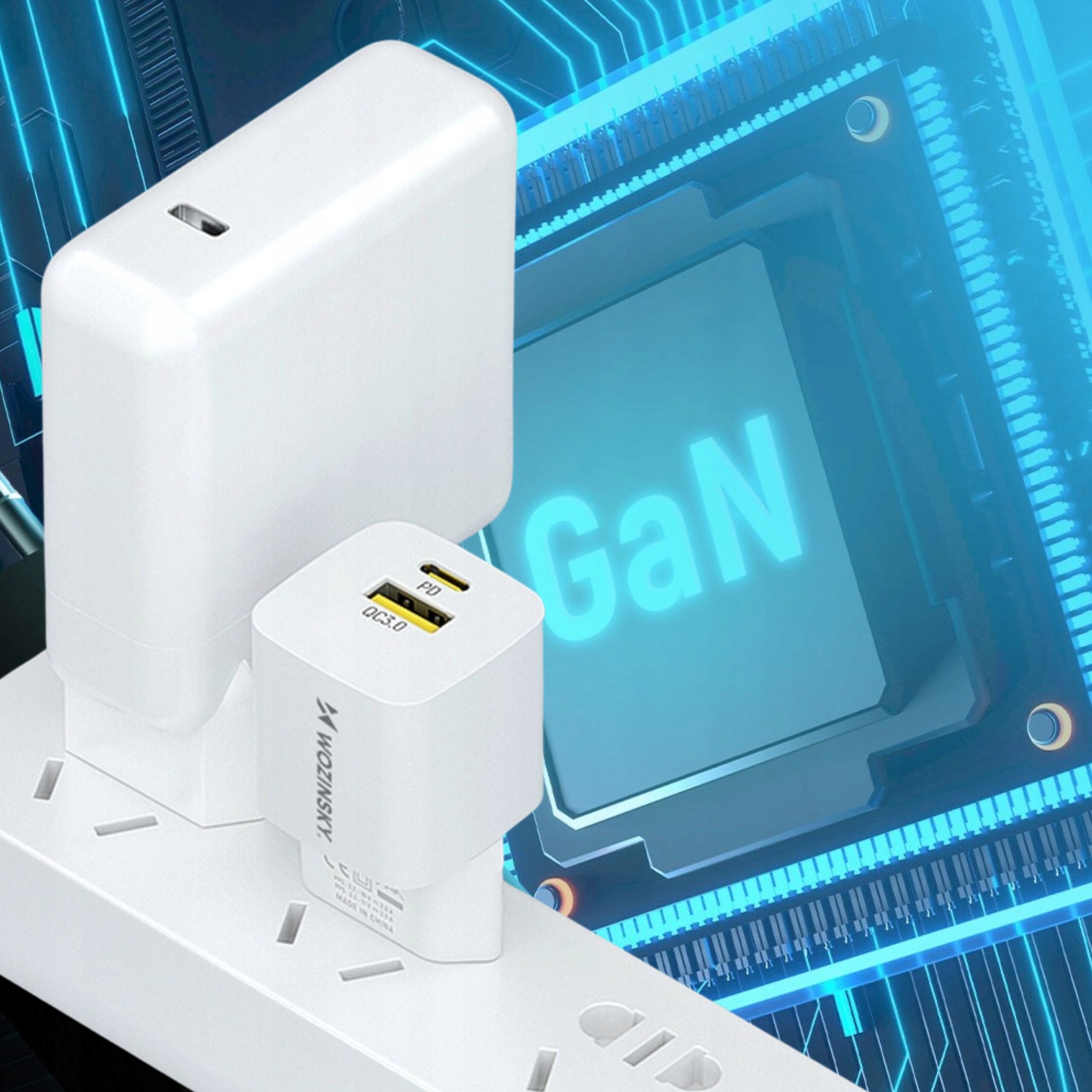 Na obrazie widoczne są dwie białe ładowarki podłączone do listwy zasilającej, z widocznymi portami USB-A i USB-C. W tle znajduje się grafika z napisem \'GaN\'.