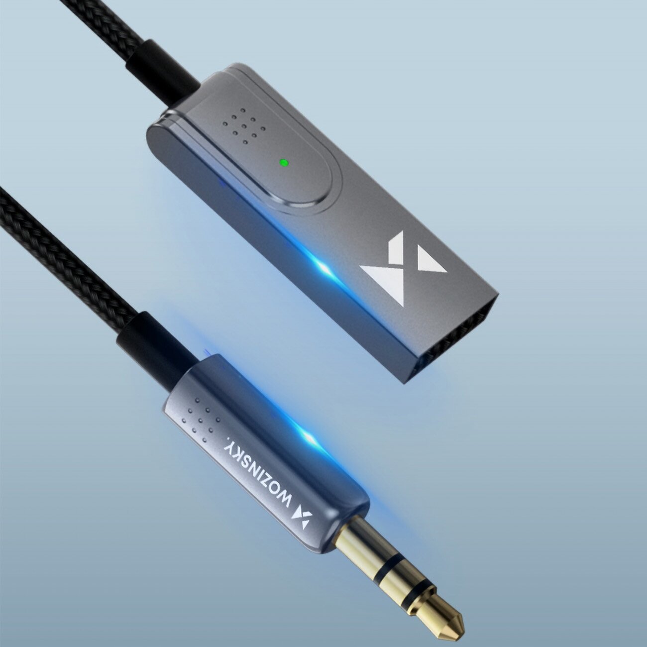 Na obrazie widoczny jest transmiter Bluetooth z metaliczną obudową i logo w postaci dwóch trójkątów. Obok znajduje się kabel z wtykiem jack, na którym widnieje napis \'WONZINSKY\'.