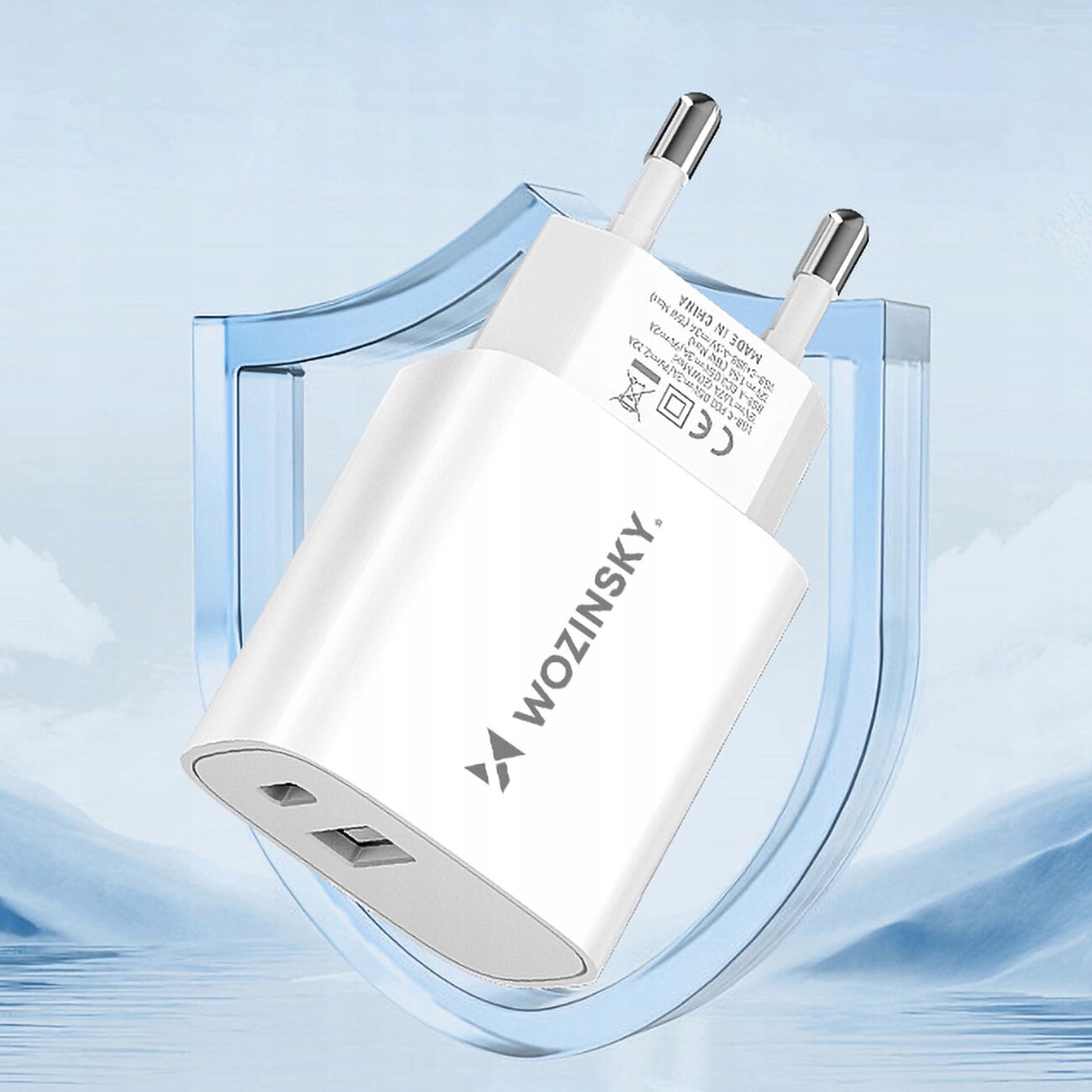 Biała ładowarka sieciowa z logo \'WOZINSKY\' posiada dwa porty: USB-A i USB-C. W tle widoczny jest niebieski kształt przypominający tarczę na tle nieba.