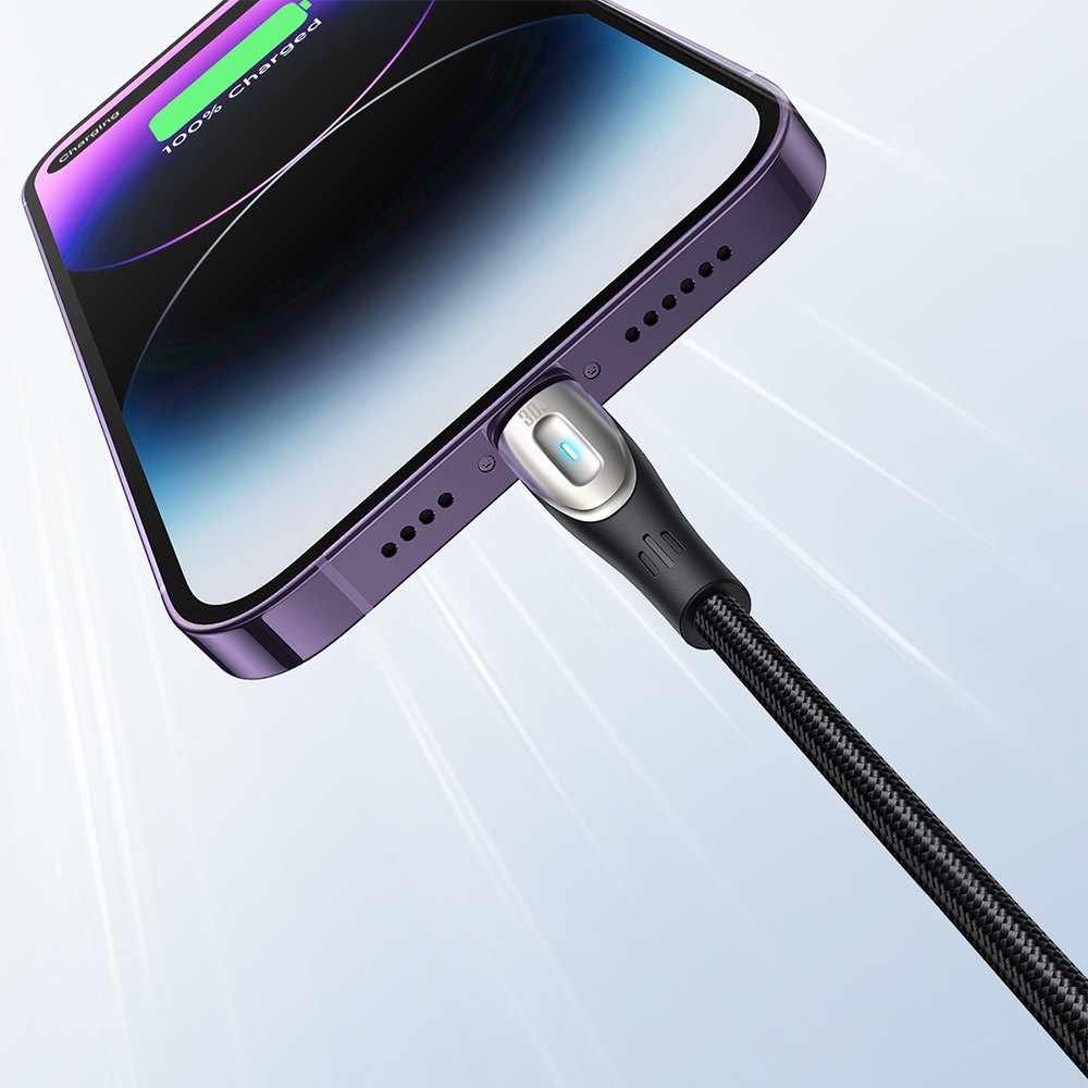 Smartfon w kolorze fioletowym jest podłączony do kabla z metaliczną końcówką, na której świeci się niebieska dioda. Na ekranie telefonu widoczny jest wskaźnik naładowania baterii z napisem \'100% Charged\'.