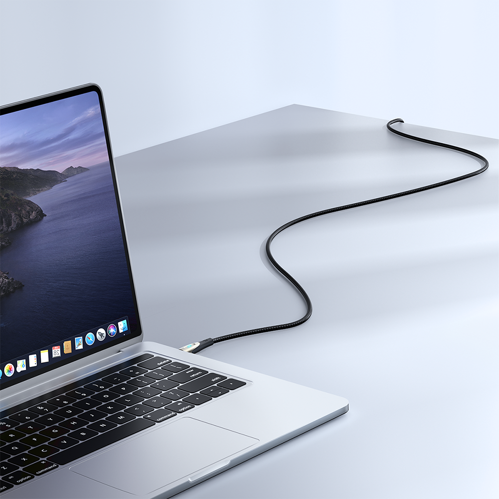 Na obrazie widoczny jest laptop z otwartym ekranem, do którego podłączony jest czarny kabel. Kabel biegnie po powierzchni stołu, tworząc łagodny łuk.