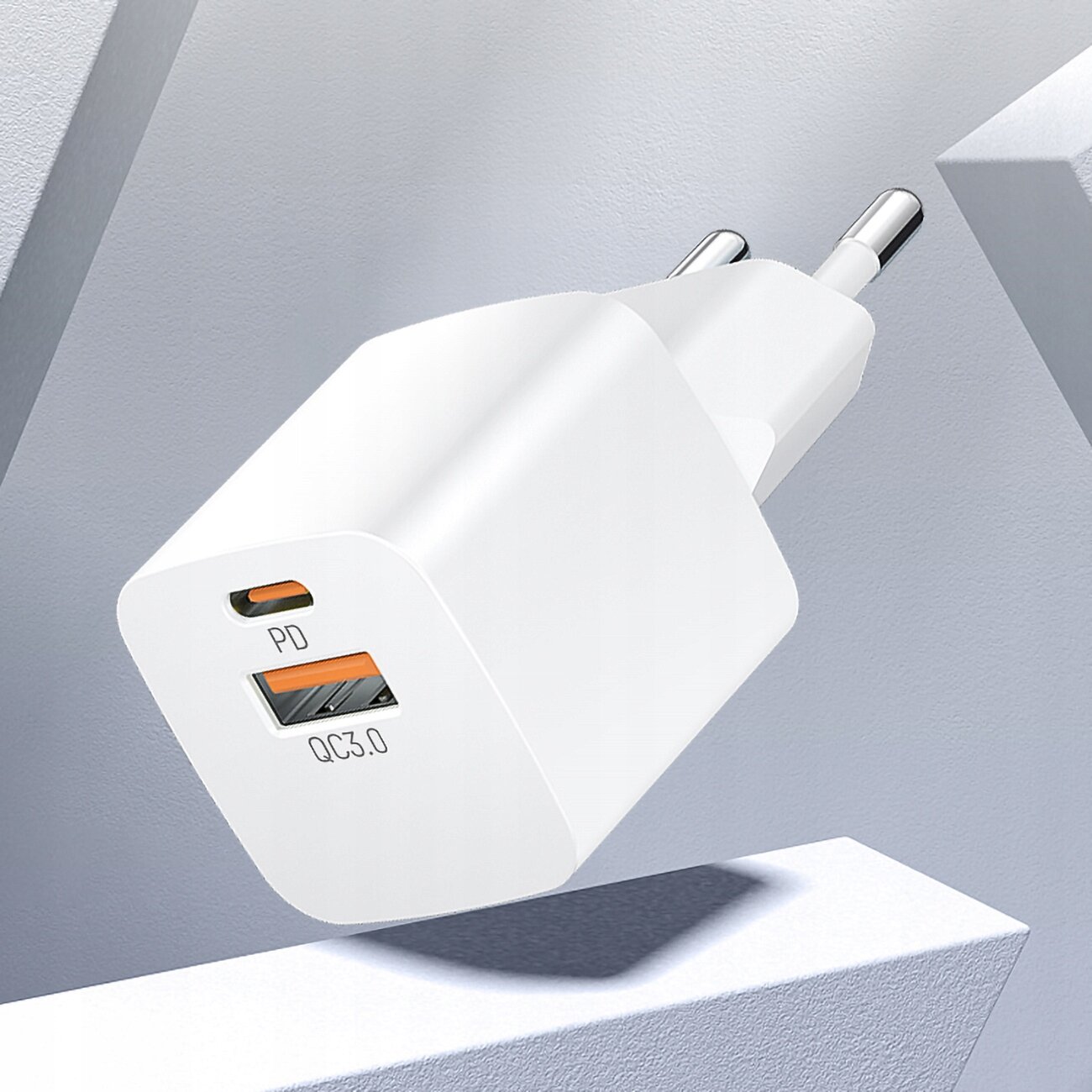 Biała ładowarka sieciowa z dwoma portami: USB-C oznaczonym jako \'PD\' i USB oznaczonym jako \'QC3.0\'. Ładowarka ma dwa metalowe bolce do podłączenia do gniazdka.