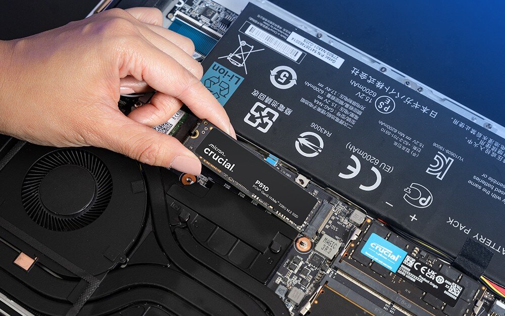 Dysk CRUCIAL P510 Dysk 'crucial P510' leży na ciemnym blacie, w tle rozmazany pad do konsoli i obudowa, pojemność