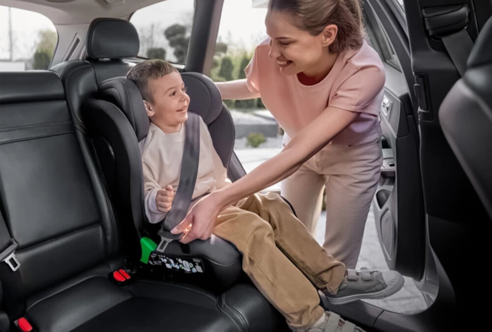 Fotelik samochodowy LIONELO Neal i-Size 100-150 cm (15-36 kg) Szary wnętrze samochodu dziecko siedzi w foteliku osoba przypina pasy bezpieczeństwa bezpieczeństwo wygoda wszechstronne zastosowanie