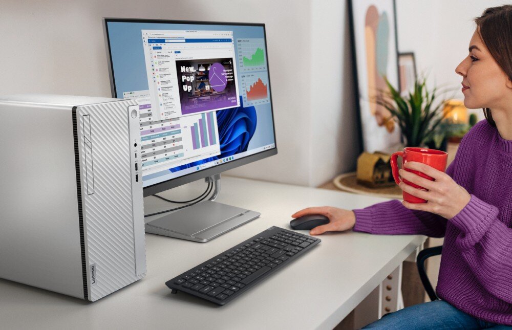 Komputer LENOVO IdeaCentre Tower 14IRR9 Kobieta w fioletowym swetrze siedzi przy biurku z kubkiem w dłoni, patrzy na monitor, obok którego stoi srebrny komputer stacjonarny z falistym frontem i pionowym panelem z portami oraz napędem optycznym, opis