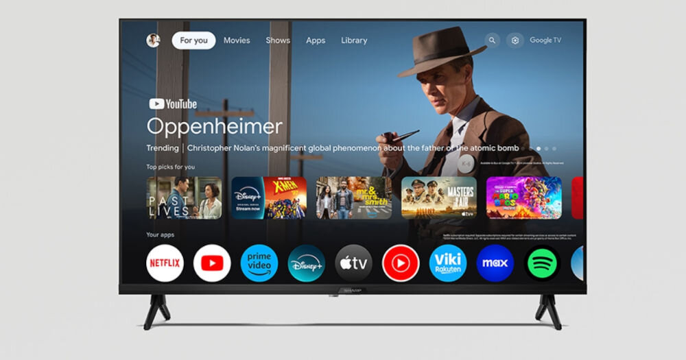 Telewizor wyświetla ekran główny z aplikacjami takimi jak YouTube, Netflix, Prime Video, Disney+, Apple TV, Viki, Max i Spotify. Na ekranie widoczny jest film \'Oppenheimer\' oraz różne rekomendacje filmowe i serialowe.