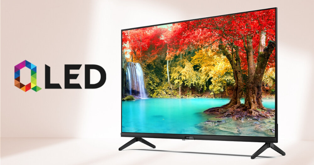 Telewizor wyświetla obraz z kolorowym krajobrazem przedstawiającym wodospad i drzewa w jesiennych barwach. Obok telewizora widoczne jest logo z napisem \'QLED\'.