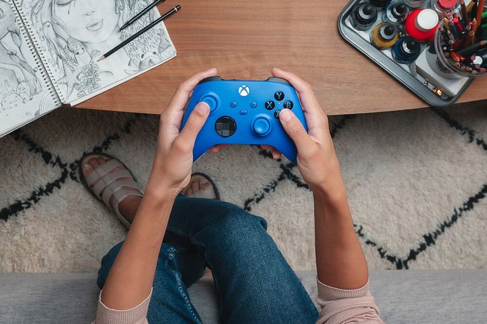 Kontroler MICROSOFT Xbox - kontroler od góry trzymany w ręku na tle dywanu