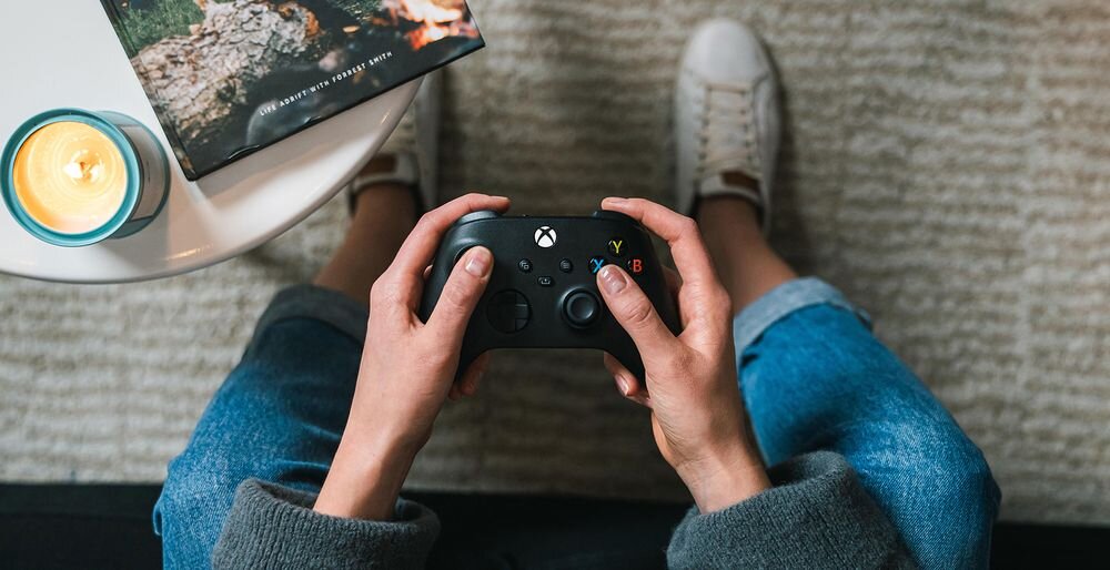 Kontroler MICROSOFT Xbox - kontroler od góry trzymany w ręku na tle dywanu