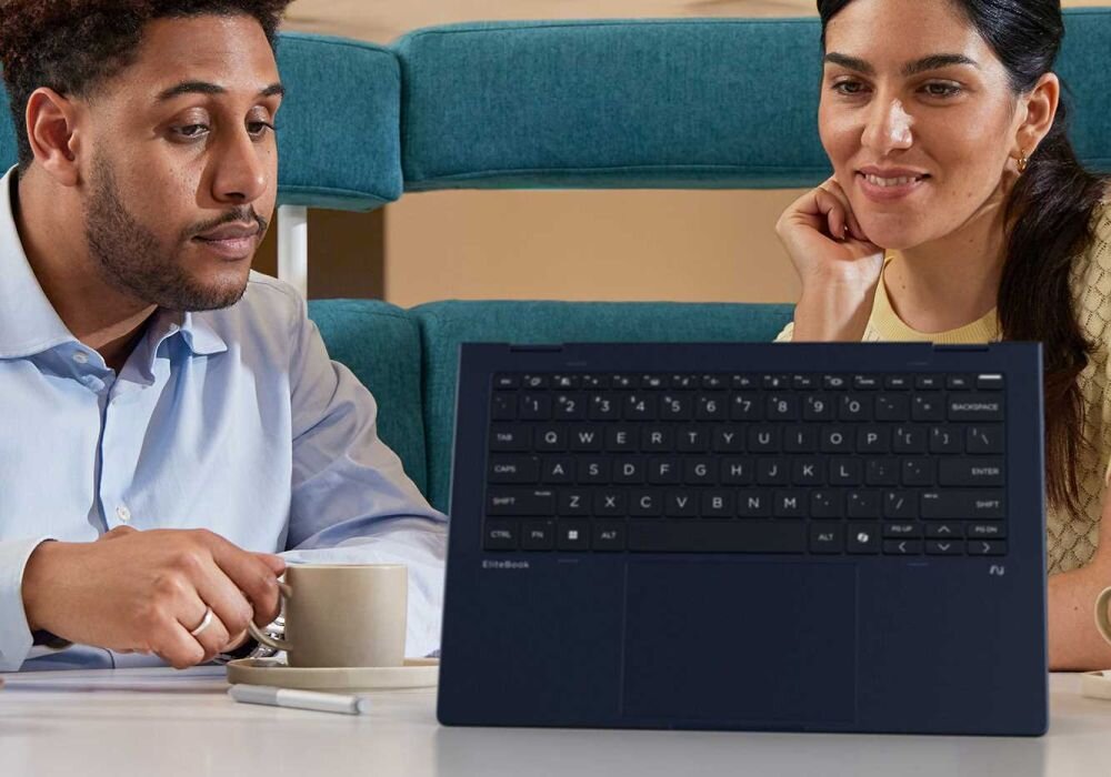 Dwóch profesjonalistów współpracujących przy laptopie HP EliteBook X Flip, mężczyzna w niebieskiej koszuli i kobieta w żółtym swetrze siedzą na turkusowej sofie, widoczna czarna klawiatura QWERTY w trybie dotykowym. - Opis serii EliteBook X Flip G1i