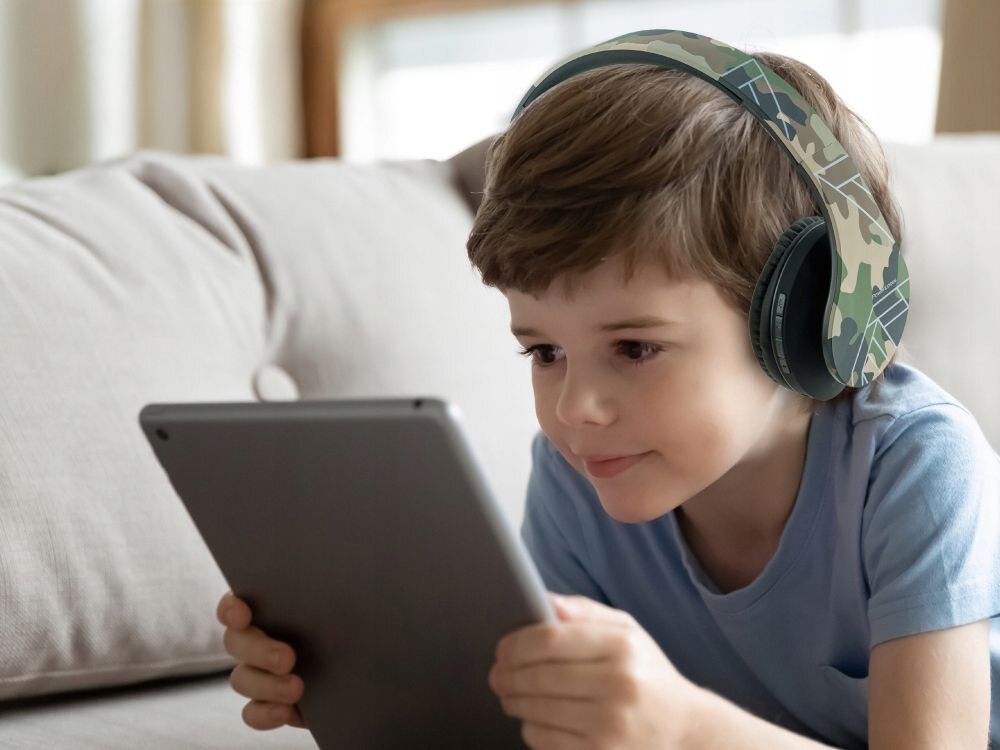 Słuchawki nauszne POWERLOCUS P2 Kids dla dzieci wygodne bezpieczne użytkowanie, dziecko z założonymi słuchawkami nausznymi trzymające tablet