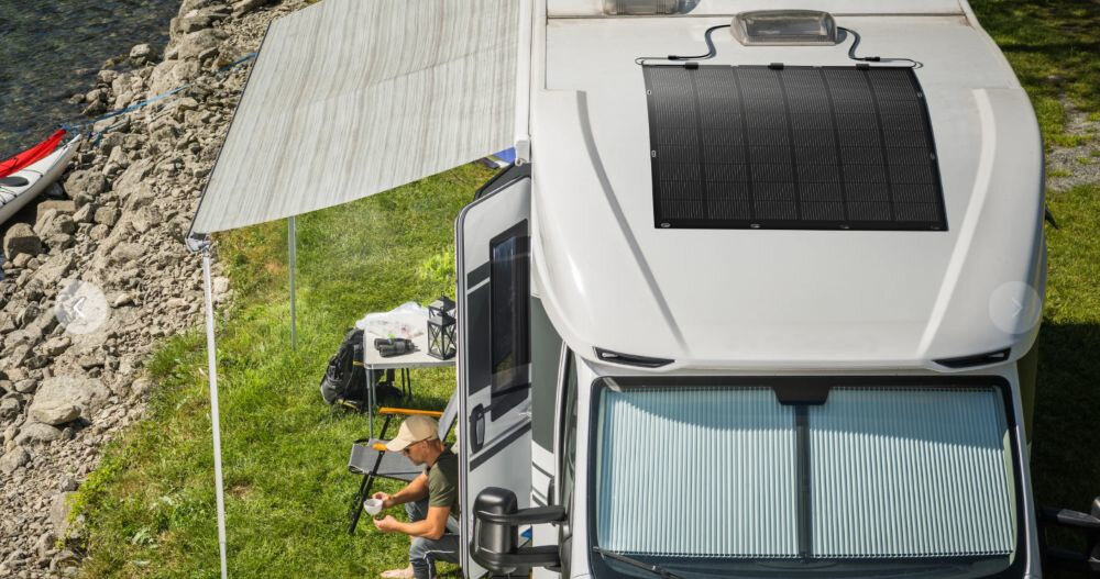 Panel fotowoltaiczny ANKER Solix FS20 900W kamper panel zamontowany na dachu w tle osoba siedzi z filiżanką trawa woda kajak efektywne źródło zasilania energia ze słońca niezależność energetyczna