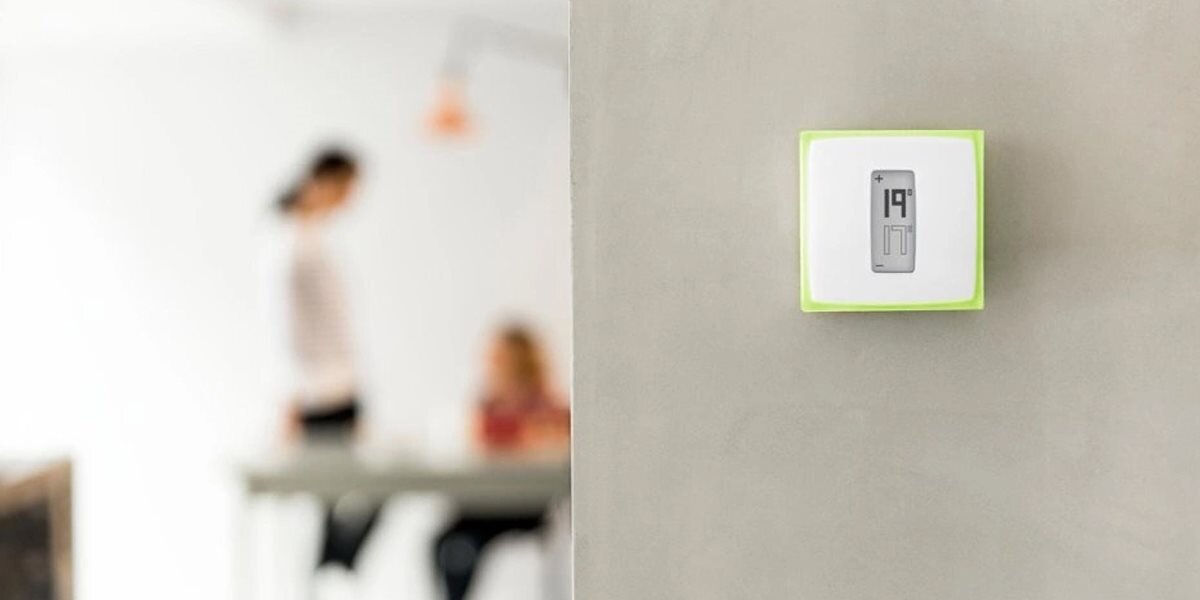 Termostat NETATMO OTH, kocioł, monitorowanie, auto-care, aplikacja, termostat na ścianie w tle 2 osoby w pomieszczeniu
