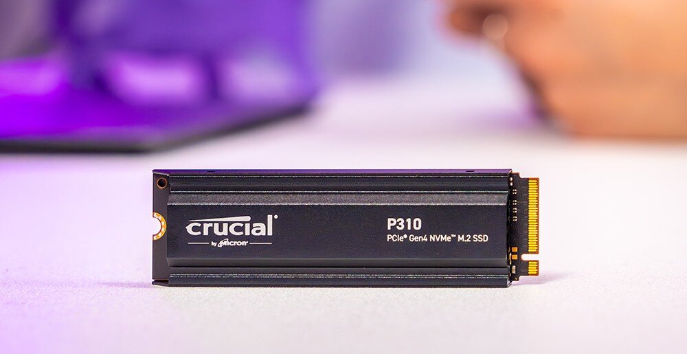 Dysk CRUCIAL P310 Dysk SSD z napisem 'crucial P310 PCIe Gen4 NVMe M.2 SSD' ustawiony pionowo na jasnym blacie, w tle rozmyte kształty, konstrukcja, działanie