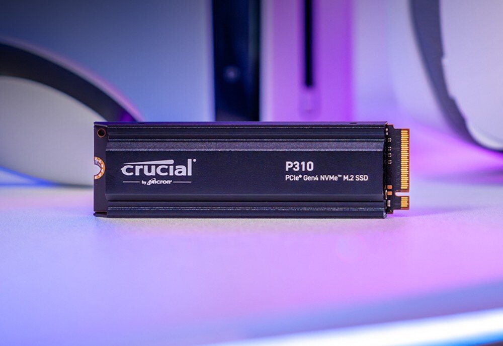 Dysk CRUCIAL P310 Dysk SSD z napisem 'crucial P310 PCIe Gen4 NVMe M.2 SSD' leży na jasnej powierzchni, w tle konsola i kontroler, energooszczędność