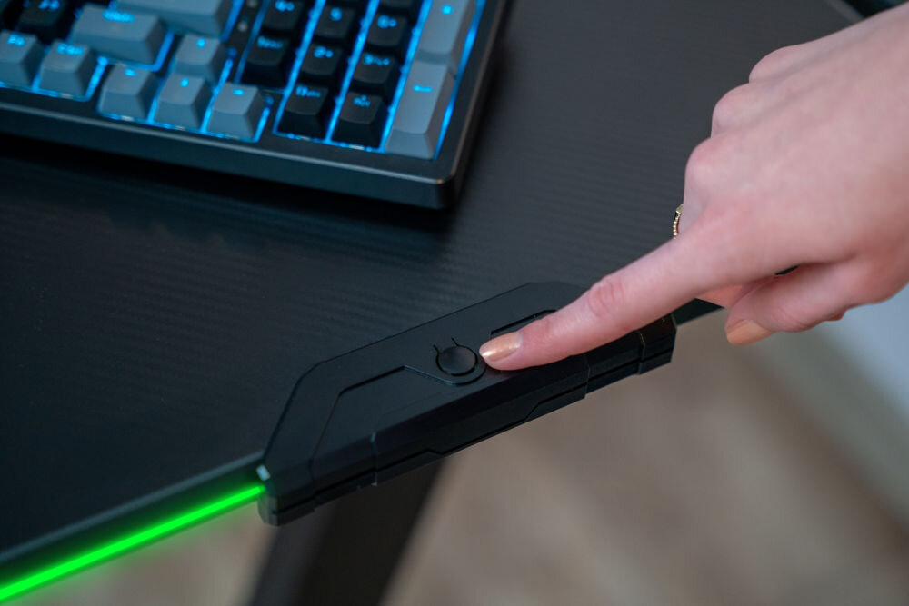 Biurko MAD DOG GD100K Zbliżenie na dłoń naciskającą przycisk sterowania oświetleniem LED na krawędzi blatu biurka gamingowego.
