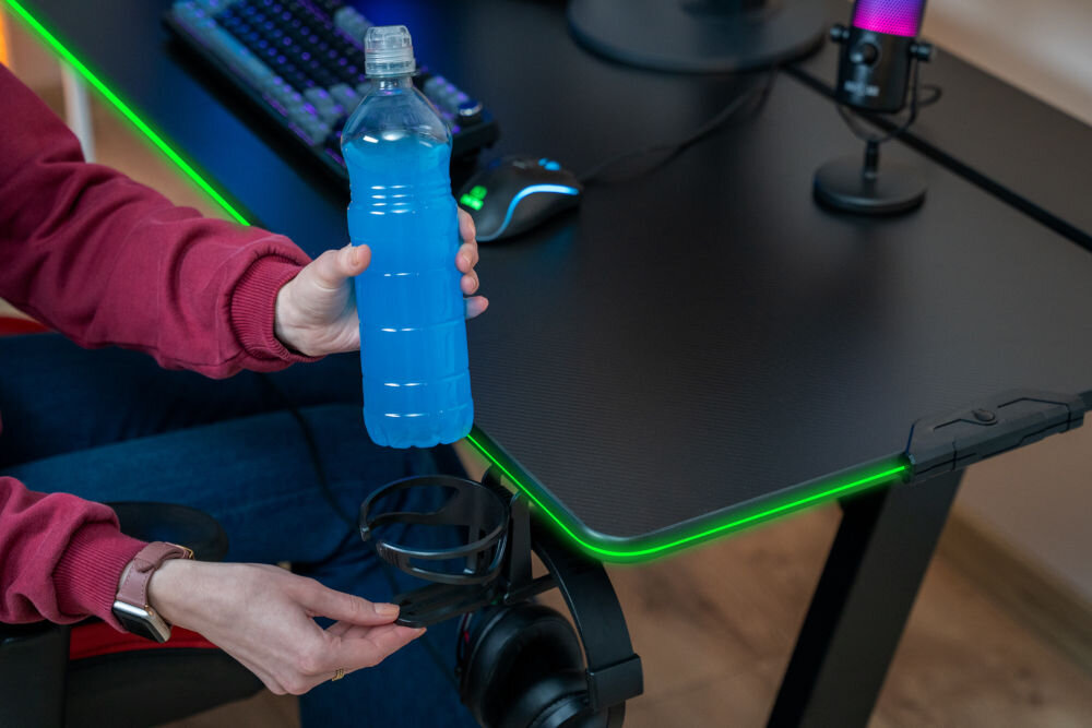Biurko MAD DOG GD100K Osoba wkładająca butelkę z napojem do dedykowanego uchwytu zamontowanego przy krawędzi biurka gamingowego MAD DOG.
