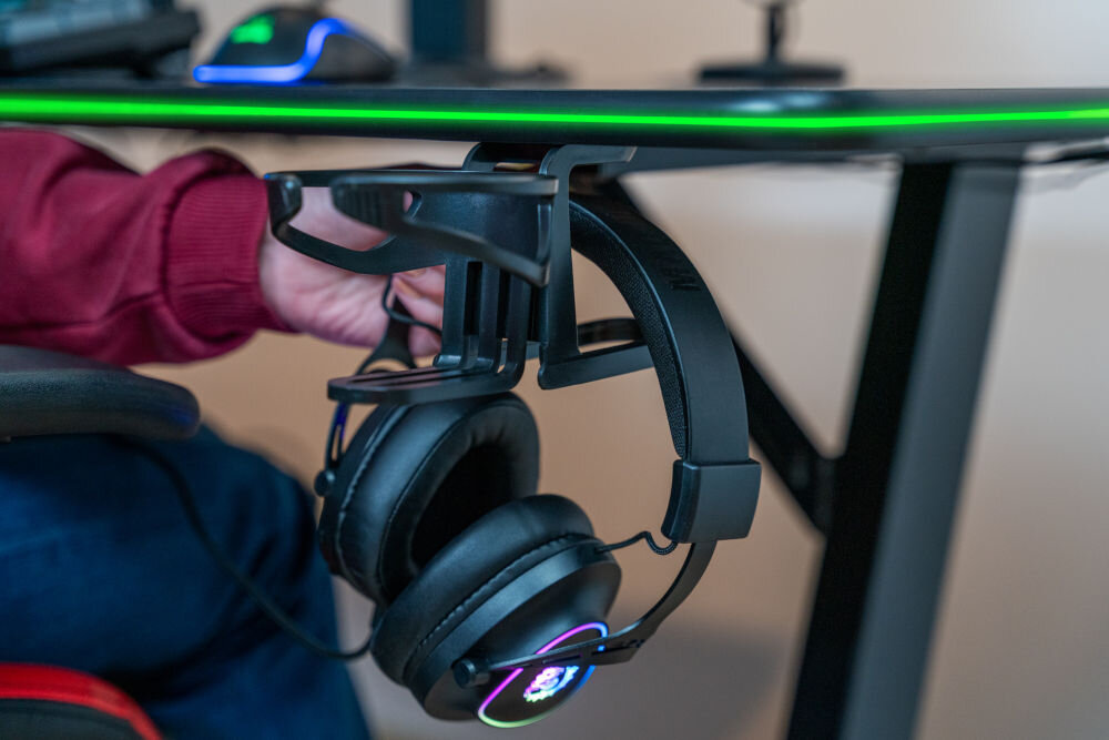 Biurko MAD DOG GD100K Słuchawki gamingowe zawieszone na zintegrowanym uchwycie pod blatem czarnego biurka dla graczy.