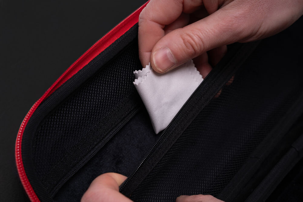 Etui MAD DOG PPA500K ze szkłem hartowanym i ściereczką do czyszczenia ekranu PlayStation Portal w zestawie Zbliżenie na dłoń wkładającą małą, białą ściereczkę z mikrofibry do wewnętrznej kieszeni zapinanej na zamek błyskawiczny w otwartym, czarnym etui.