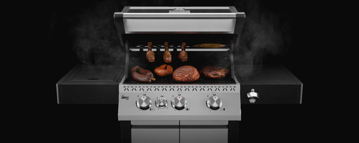 Grill gazowy z otwartą pokrywą, na ruszcie znajdują się różne rodzaje mięsa. Grill posiada cztery pokrętła i boczny palnik, a w tle widoczna jest para.