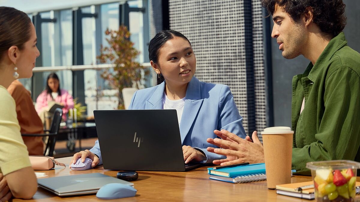 HP 400 Quiet Bluetooth® adapter USB-A Energooszczędny mechanizm 24 miesięcy na jednej baterii - Spotkanie biznesowe przy stole, na którym kobieta w niebieskiej marynarce obsługuje laptopa i fioletową mysz komputerową, rozmawiając ze współpracownikami.