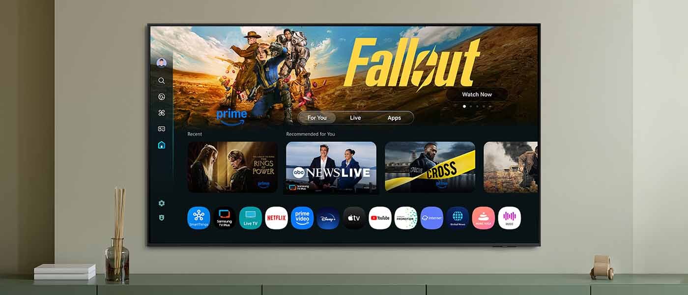 1400x600 one ui tizen one ui tizen mo eu pc Ekran telewizora smart TV Samsung QLED Q7F2AU 2025 z systemem operacyjnym Tizen, widziany od przodu, powieszony na szarej ścianie, a na nim wyświetlane treści i aplikacje.