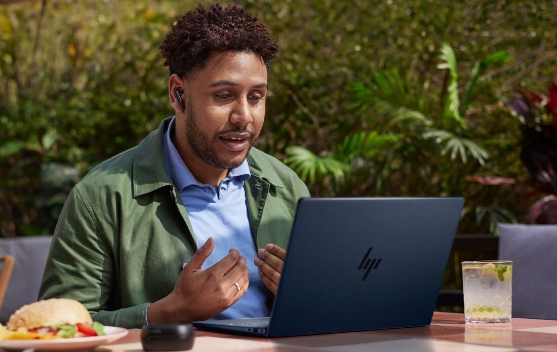 Mężczyzna pracujący na laptopie HP EliteBook w ogrodzie z zielonymi roślinami w tle.