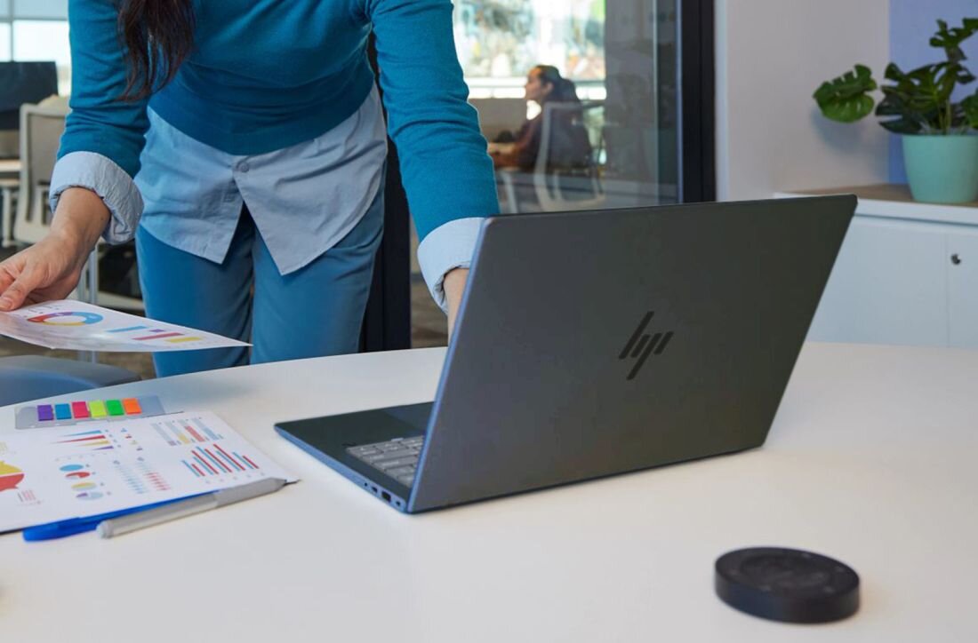 Kobieta w niebieskim swetrze pracująca przy laptopie HP z wykresami i dokumentami na biurku. - Pamięć RAM LPDDR5X, dysk SSD PCIe NVMe