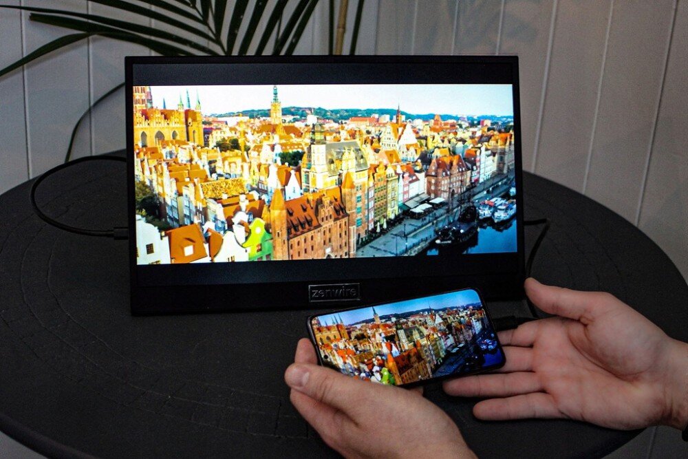 Monitor ZENWIRE M8P Monitor przenośny ustawiony na okrągłym stole, podłączony do smartfona trzymanego w dłoniach, oba ekrany pokazują panoramę miasta, przekątna, matryca, rozdzielczość, HDR