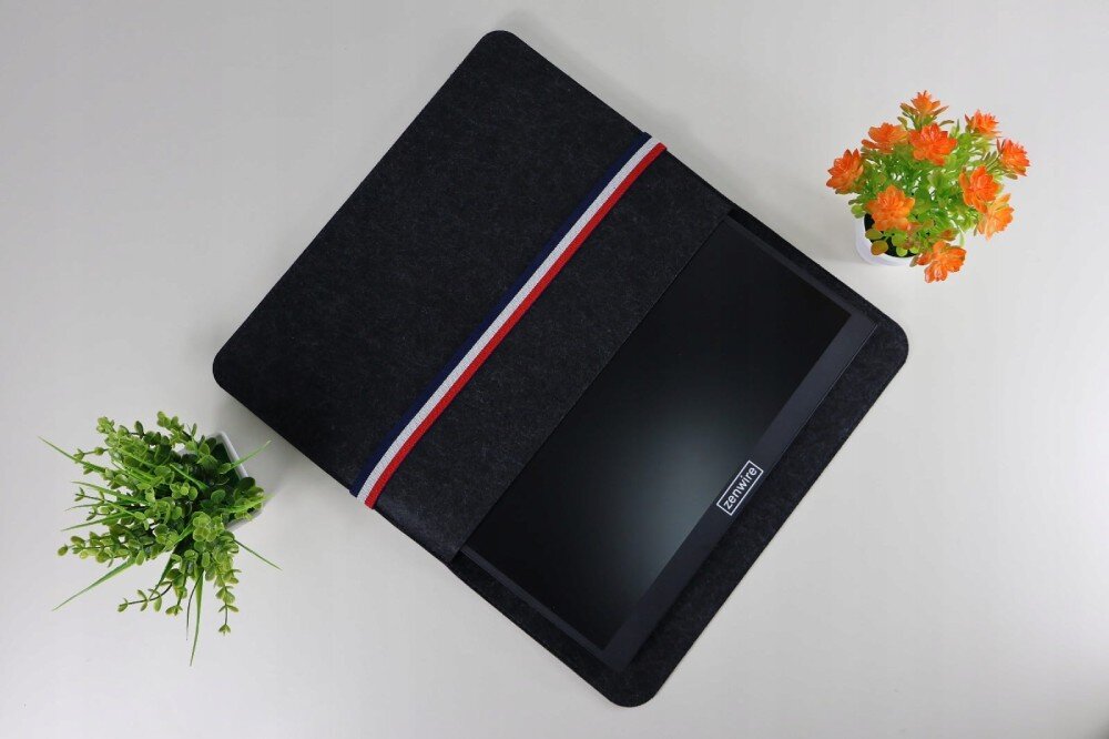 Monitor ZENWIRE M8P Monitor przenośny wsunięty w ciemne etui z paskiem w kolorach biało-czerwono-niebieskim, obok znajdują się dwie doniczki z roślinami, konstrukcja, waga, grubość, etui